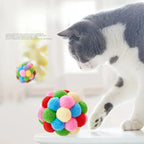 Balle de jeu interactive pour chat en pompons multicolores, devant un chat noir et blanc.