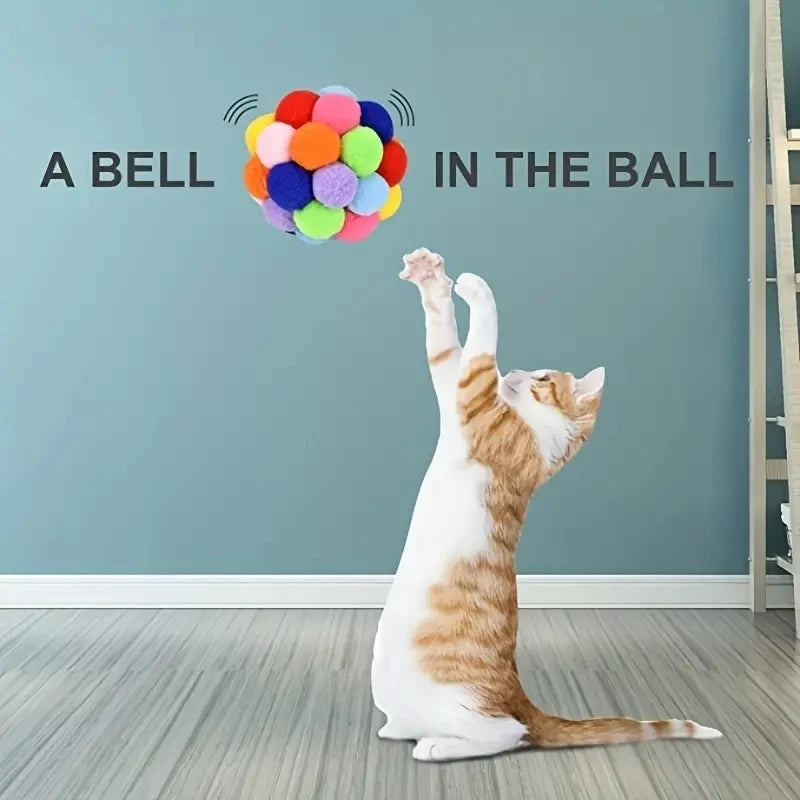 Balle de jeu interactive pour chat en pompons multicolores, près d’un chat.