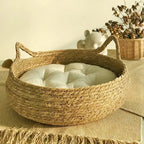 Panier pour chat en rotin rond avec coussin moelleux blanc cassé, poignées en corde.