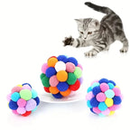 Balles de jeu pour chat en pompons multicolores, avec chat tigré à côté.